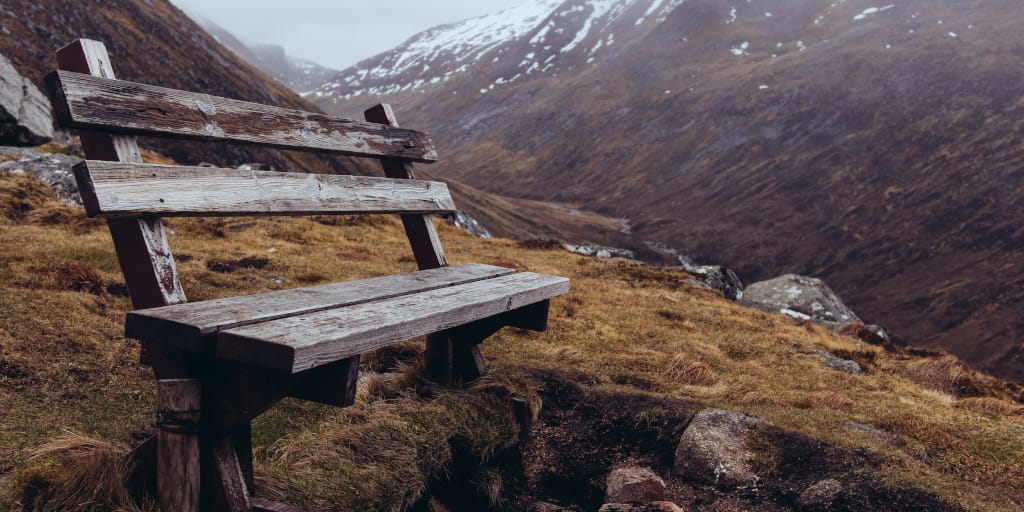 Living in the Love. Photo by Nitin Mathew on Unsplash. Shows an empty bench on a hillside.