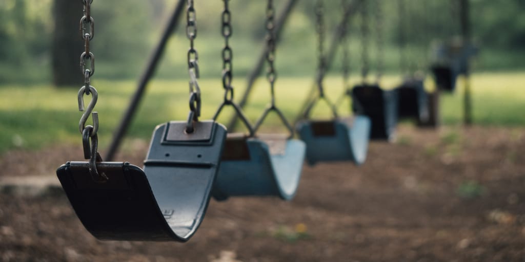 The Paracosm Girl. Photo by Aaron Burden on Unsplash. Shows a row of empty swings.